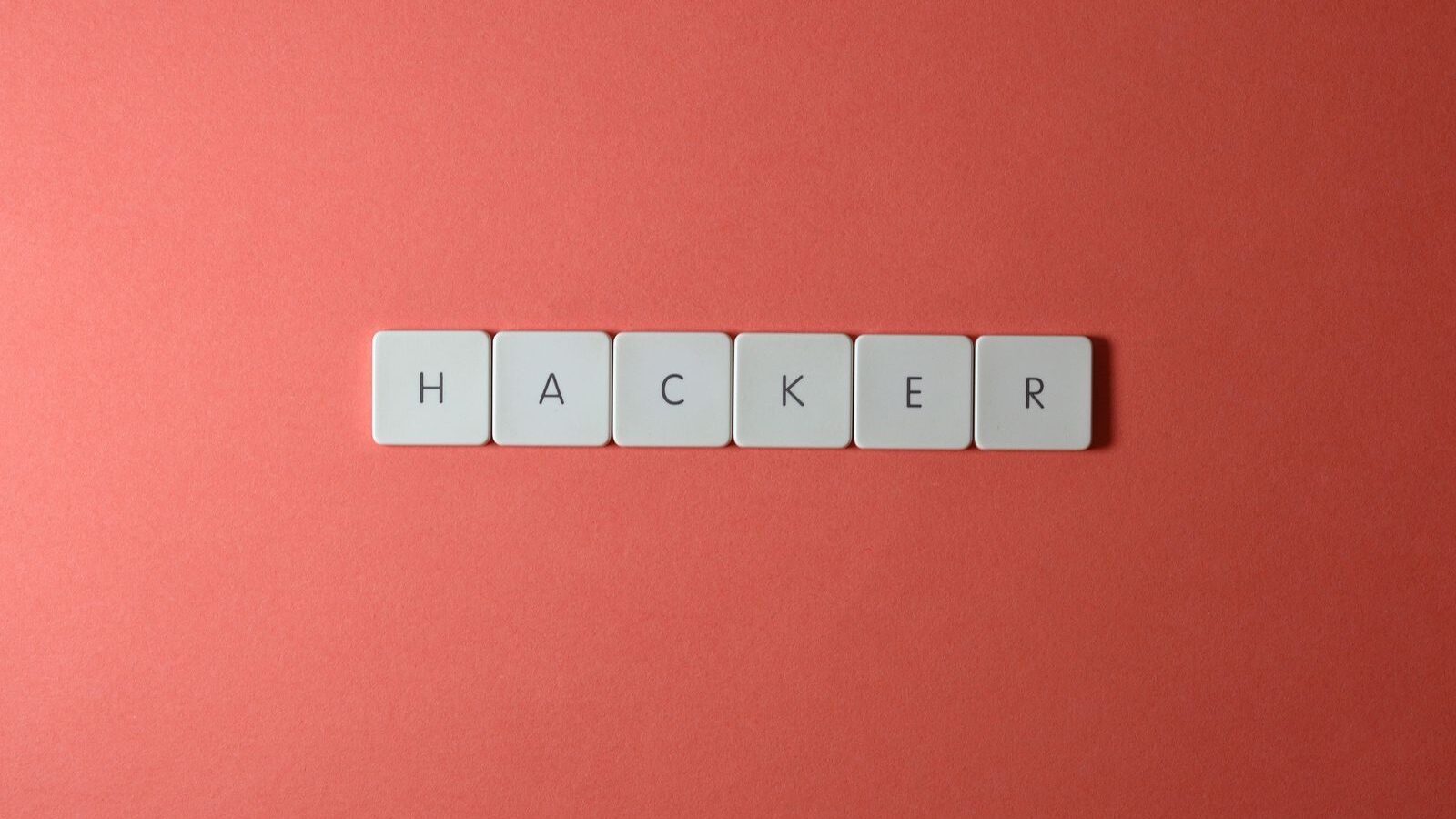 Close-up of the word 'HACKER' made with letter tiles on a red background, emphasizing cybersecurity.