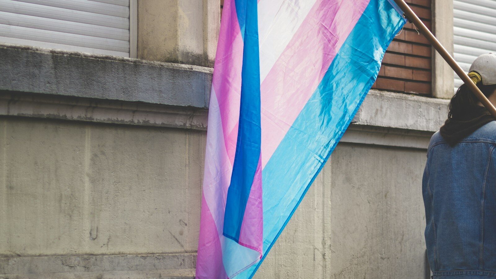 a person holding a pink and blue flag next to a building